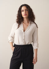 Woman wearing a white silk shirt and black trousers against a plain background