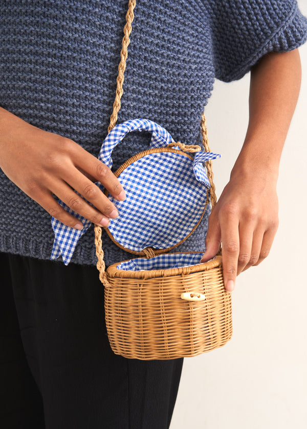 A round wicker basket with a blue gingham handle