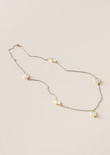 A delicate gold chain necklace featuring five irregular, organic-shaped white mother-of-pearl beads spaced along the chain, displayed on a light beige textured background.