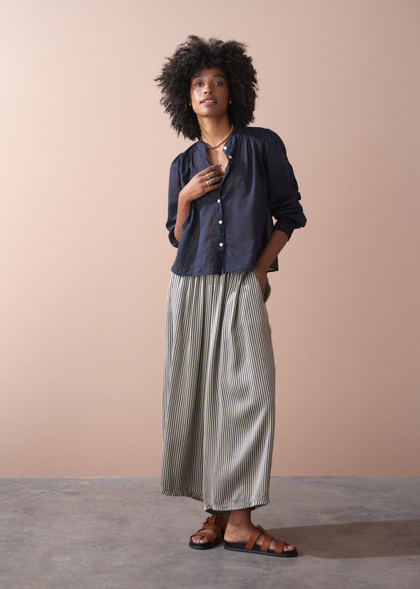 Woman wearing a dark blue button-up shirt and striped trousers against a beige background
