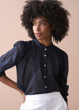 Woman wearing a navy blue blouse with white buttons against a beige background