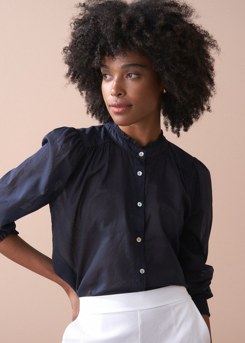 Woman wearing a navy blue blouse with white buttons against a beige background