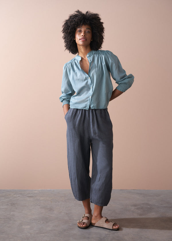 Woman wearing a light blue shirt and dark gray pants against a beige background
