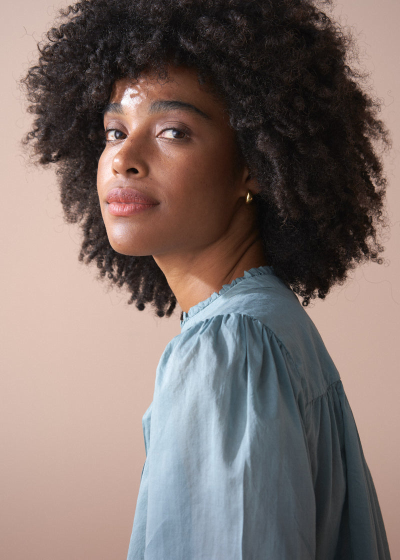 Woman with natural hair wearing a light blue shirt against a beige background
