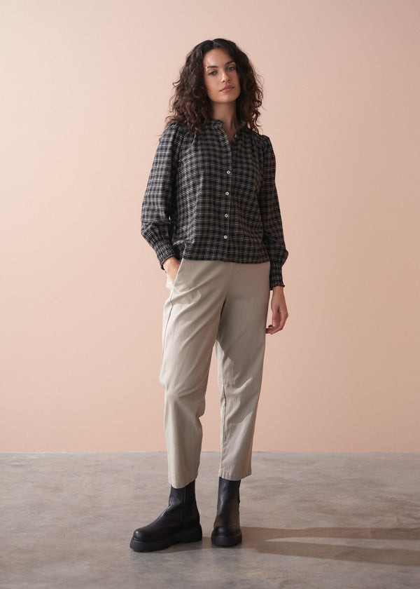 Woman wearing a checkered shirt, beige trousers, and black boots against a beige background