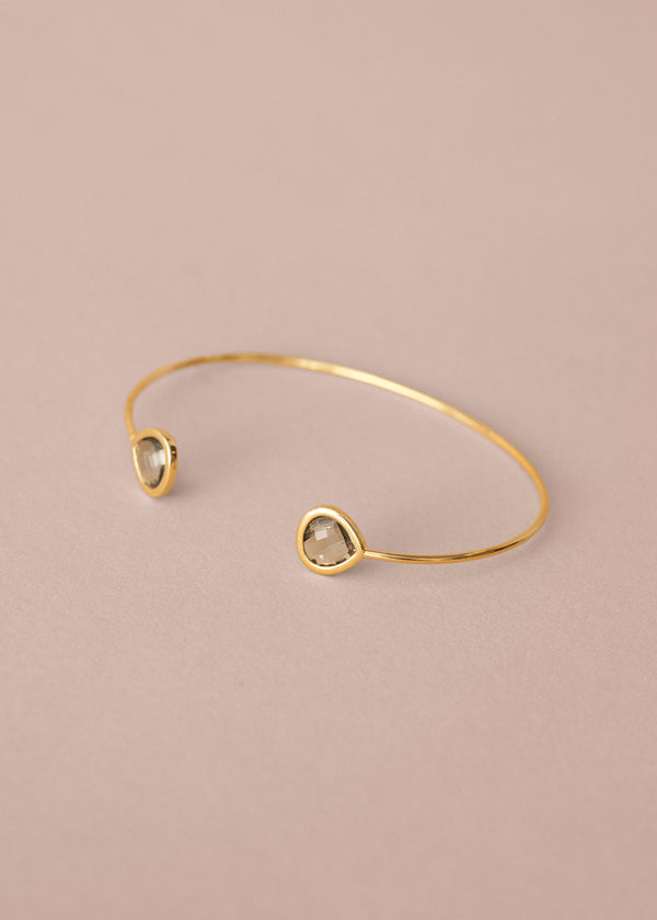 Gold bracelet with two green gemstones on a beige background