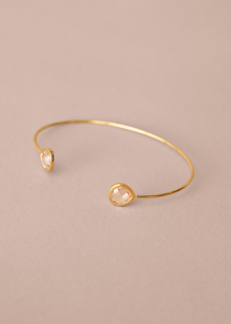 Gold bracelet with two clear gemstones on a beige background