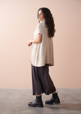 Woman wearing a white textured top and brown pants against a beige background