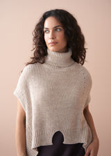 Woman wearing a beige knitted poncho against a plain background