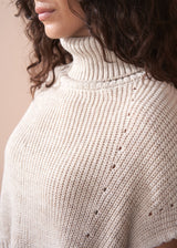 Close-up of a person wearing a beige knitted sweater with a plain background