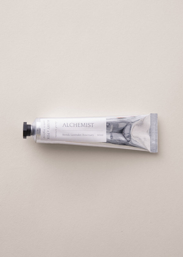 Hand cream tube labeled 'Alchemist' on a light gray background