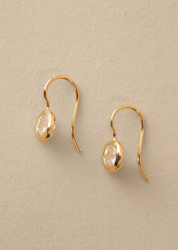 Gold earrings with clear gemstones on a beige background