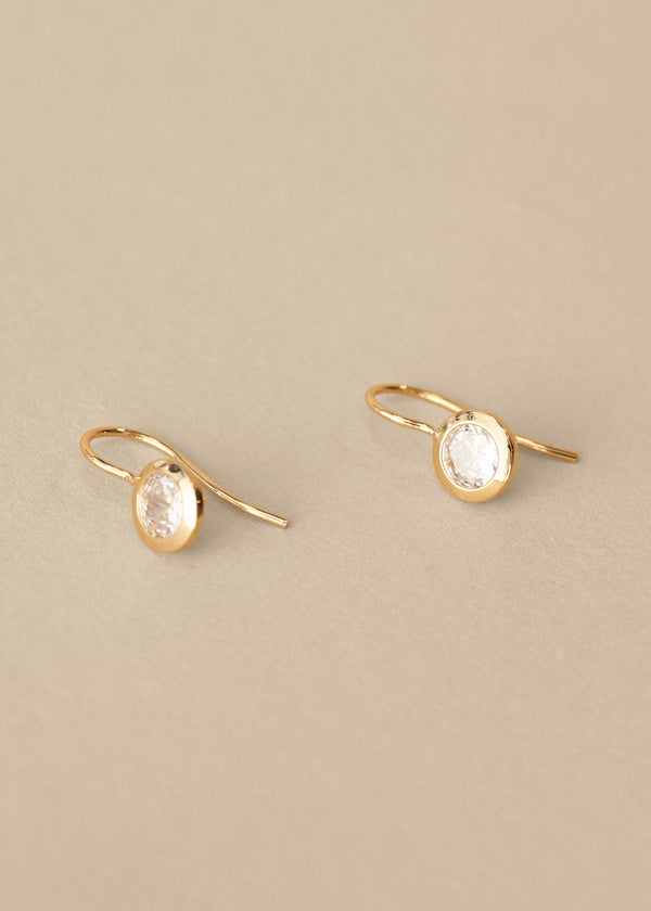 Gold earrings with clear gemstones on a beige background