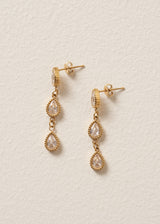 Gold earrings with teardrop-shaped gemstones on a beige background