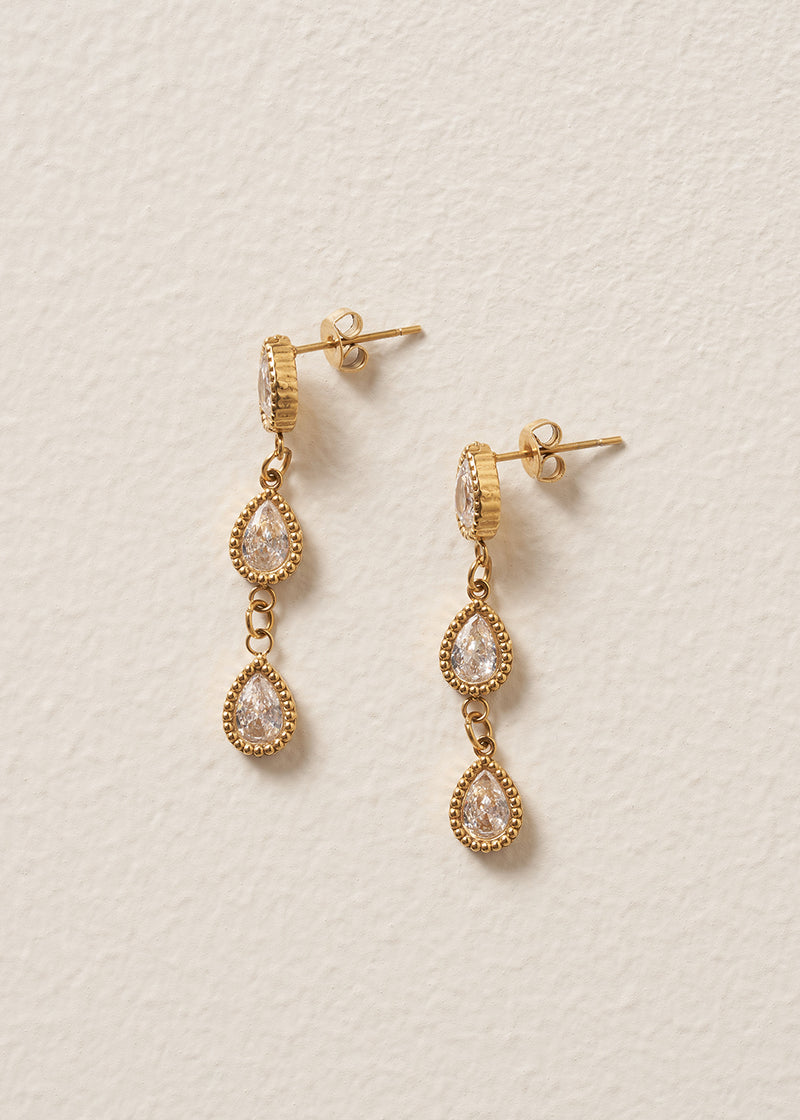 Gold earrings with teardrop-shaped gemstones on a beige background