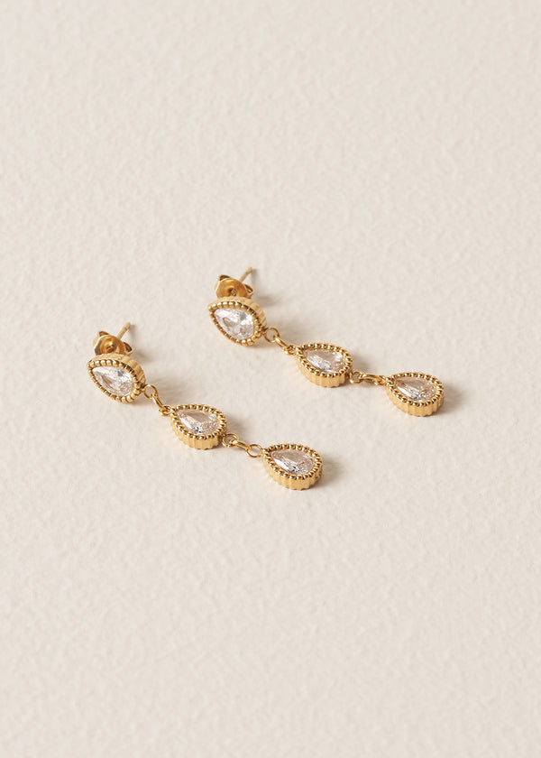 Gold earrings with clear stones on a beige background
