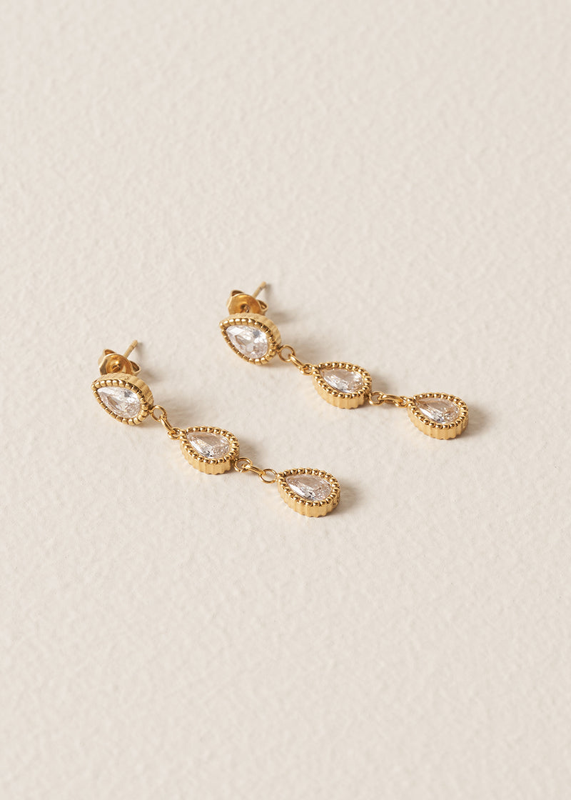 Gold earrings with clear stones on a beige background