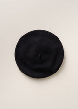 A classic black felt beret hat photographed from directly above against a clean, off-white textured background.
