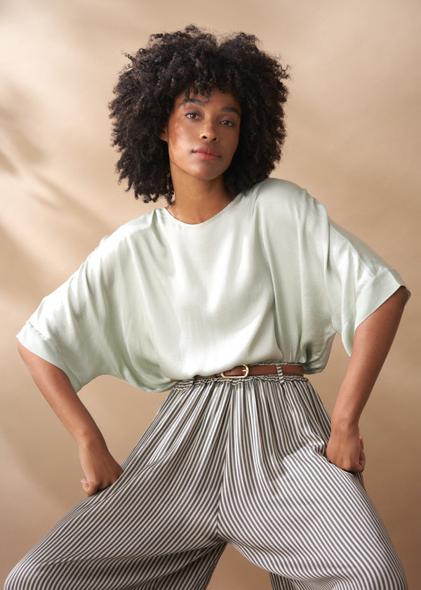 Woman wearing a light green top and striped wide leg trousers against a beige background