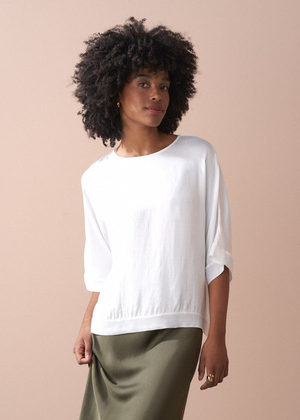 Woman wearing a white top and green satin midi skirt against a beige background