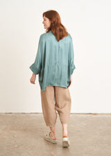 A model wearing a aqua teal blue satin overszied shirt with 3/4 sleeves and mother of pearl buttons