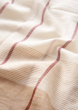 A close-up of a soft woven textile with an off-white base, thin tan horizontal stripes, and rust-red vertical lines running through it.