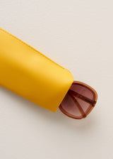Yellow sunglasses case with a brown sunglasses on a light beige background