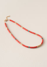 A beaded necklace with small coral-red beads, accented with metallic gold spacers and turquoise blue beads, displayed on a light beige textured background.