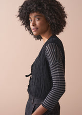 Person wearing a black textured waistcoat over a striped shirt on a beige background