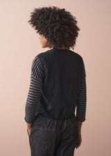 Person wearing a black textured waistcoat over a striped shirt on a beige background
