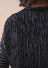 Person wearing a black textured waistcoat over a striped shirt on a beige background