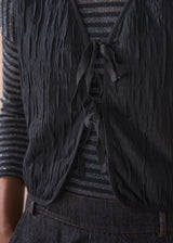 Person wearing a black textured waistcoat over a striped shirt on a beige background