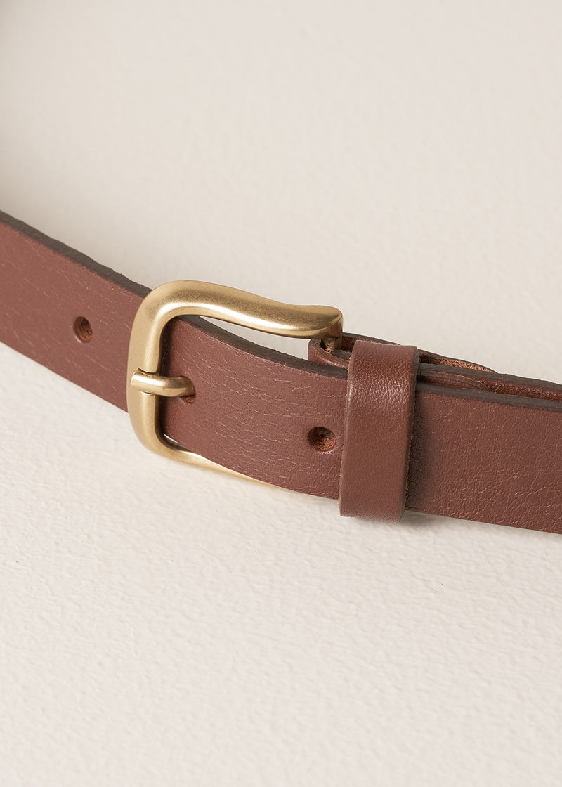 Brown leather belt with a brass buckle on a beige background