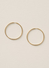 A pair of thin gold hoop earrings displayed on a textured off-white background.