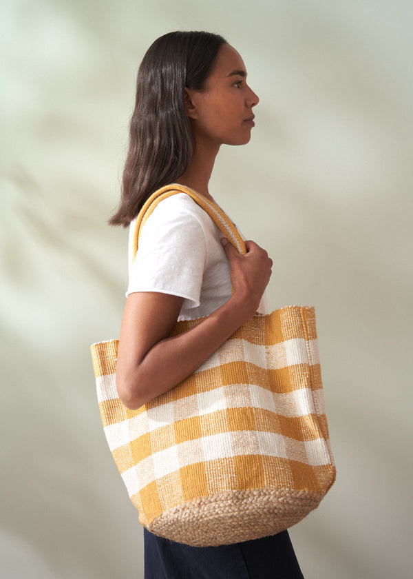 Woman holding a yellow and white striped tote bag against a plain background