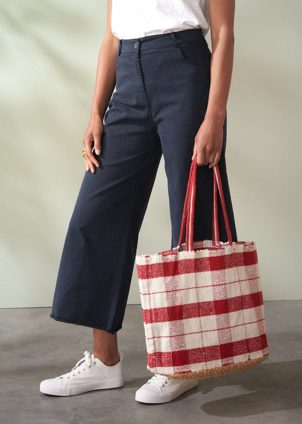 Person holding a red and white checkered bag wearing navy pants and white shoes on a neutral background