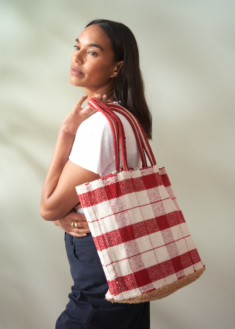Woman holding a red and white checkered bag against a plain background