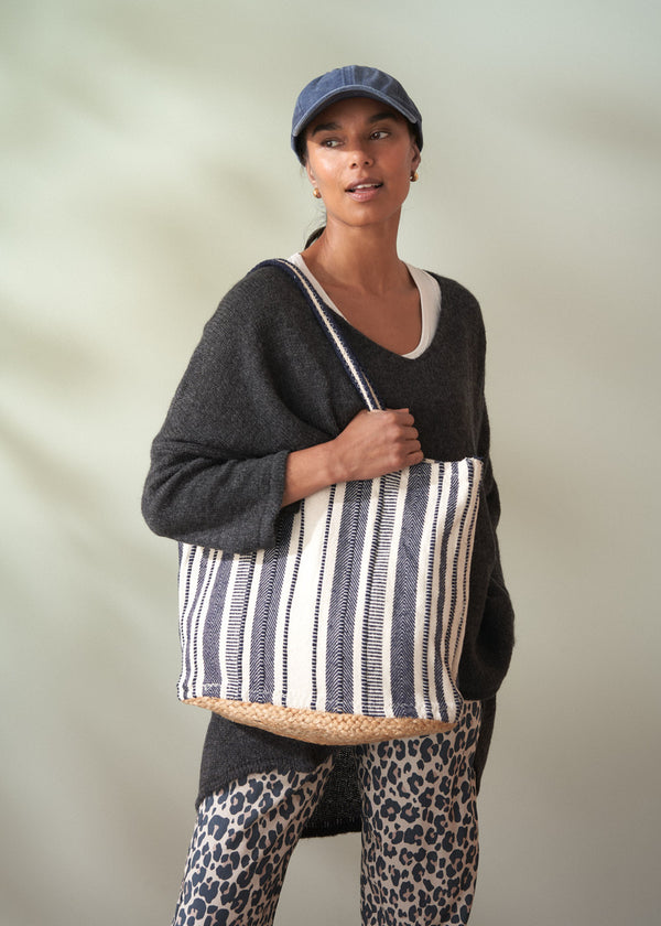 Woman holding a striped tote bag against a plain background