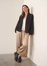 Woman wearing a oversized quilted jacket over a white top and gold trousers against a light background
