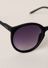 Black sunglasses with purple lenses on a light beige background