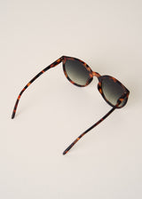 Sunglasses with tortoiseshell frame and dark lenses on a light beige background