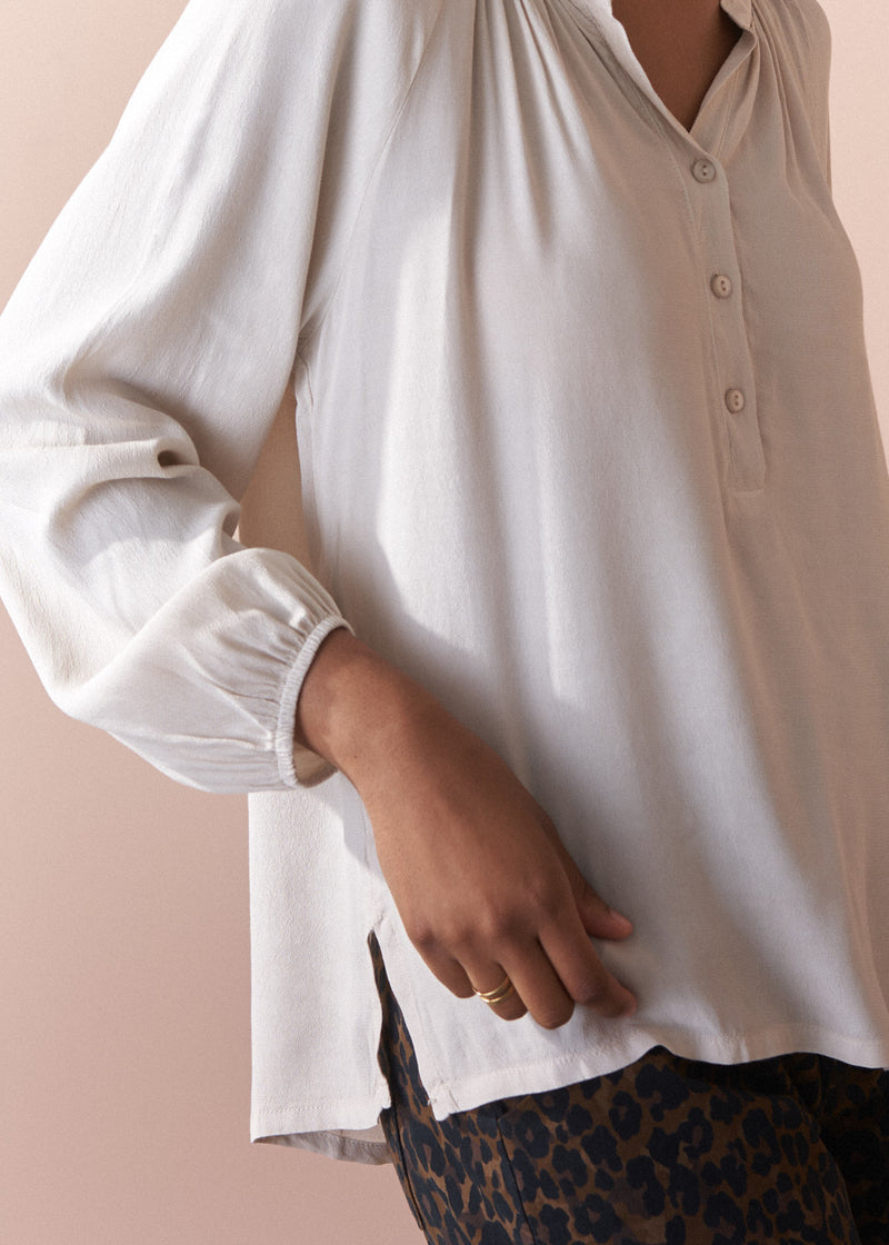 Woman wearing an oatmeal blouse against a beige background