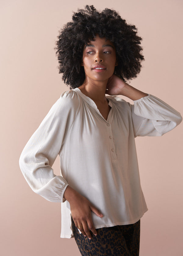 Woman wearing an oatmeal blouse against a beige background
