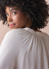 Woman wearing an oatmeal blouse against a beige background