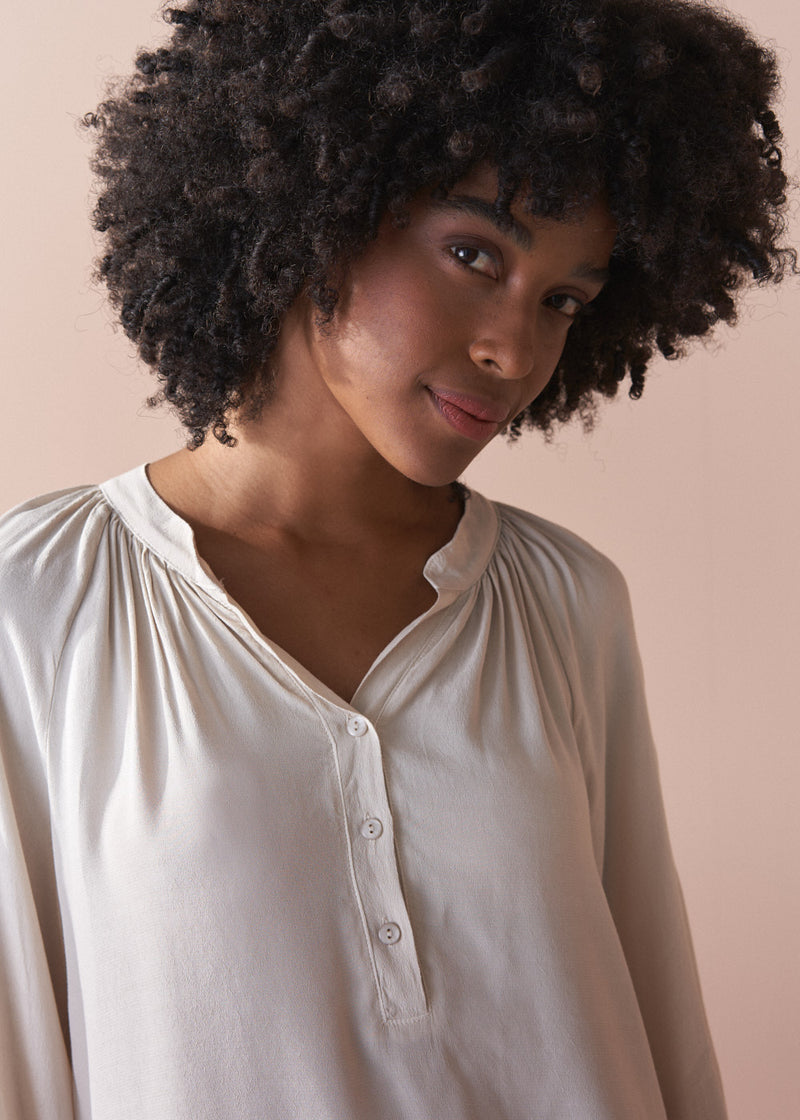 Woman wearing an oatmeal blouse against a beige background