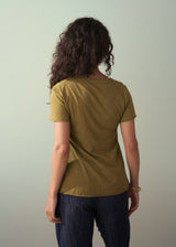 Woman wearing an olive green v-neck cotton t-shirt with blue trousers and gold bangles