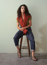Woman wearing a red jumper over an olive green v-neck cotton t-shirt, with blue trousers and sandals