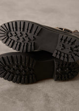 Close-up of black boots with tread pattern on a gray surface