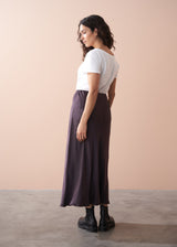 Woman wearing a white t-shirt and dark burgundy satin slip skirt against a beige background