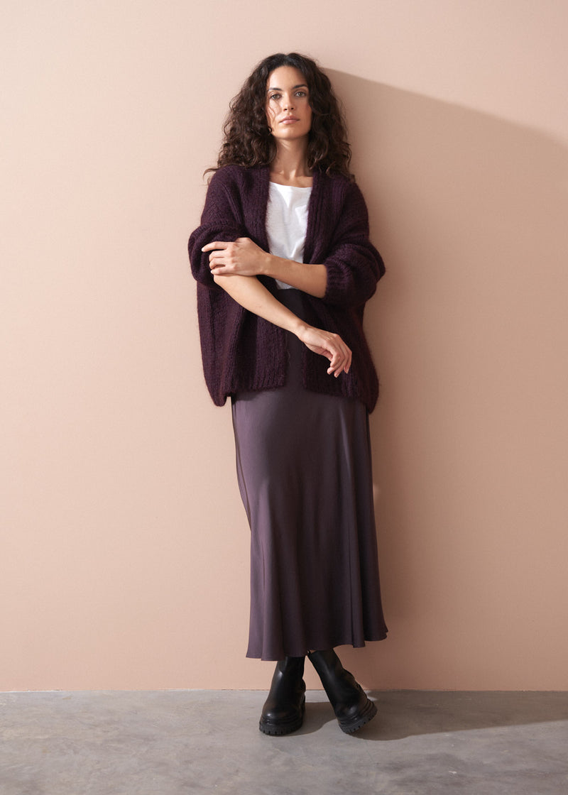 Woman wearing a white t-shirt and dark burgundy satin slip skirt against a beige background